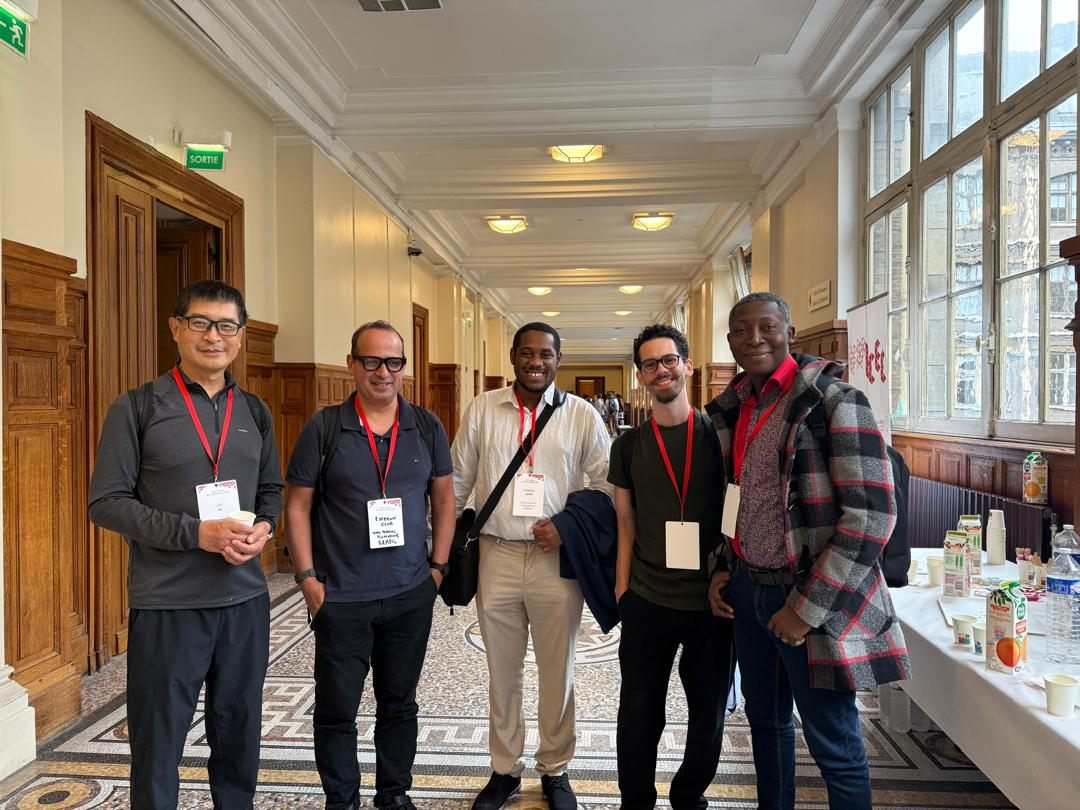 Five conference attendees with badges standing together in a long, sunlit hallway