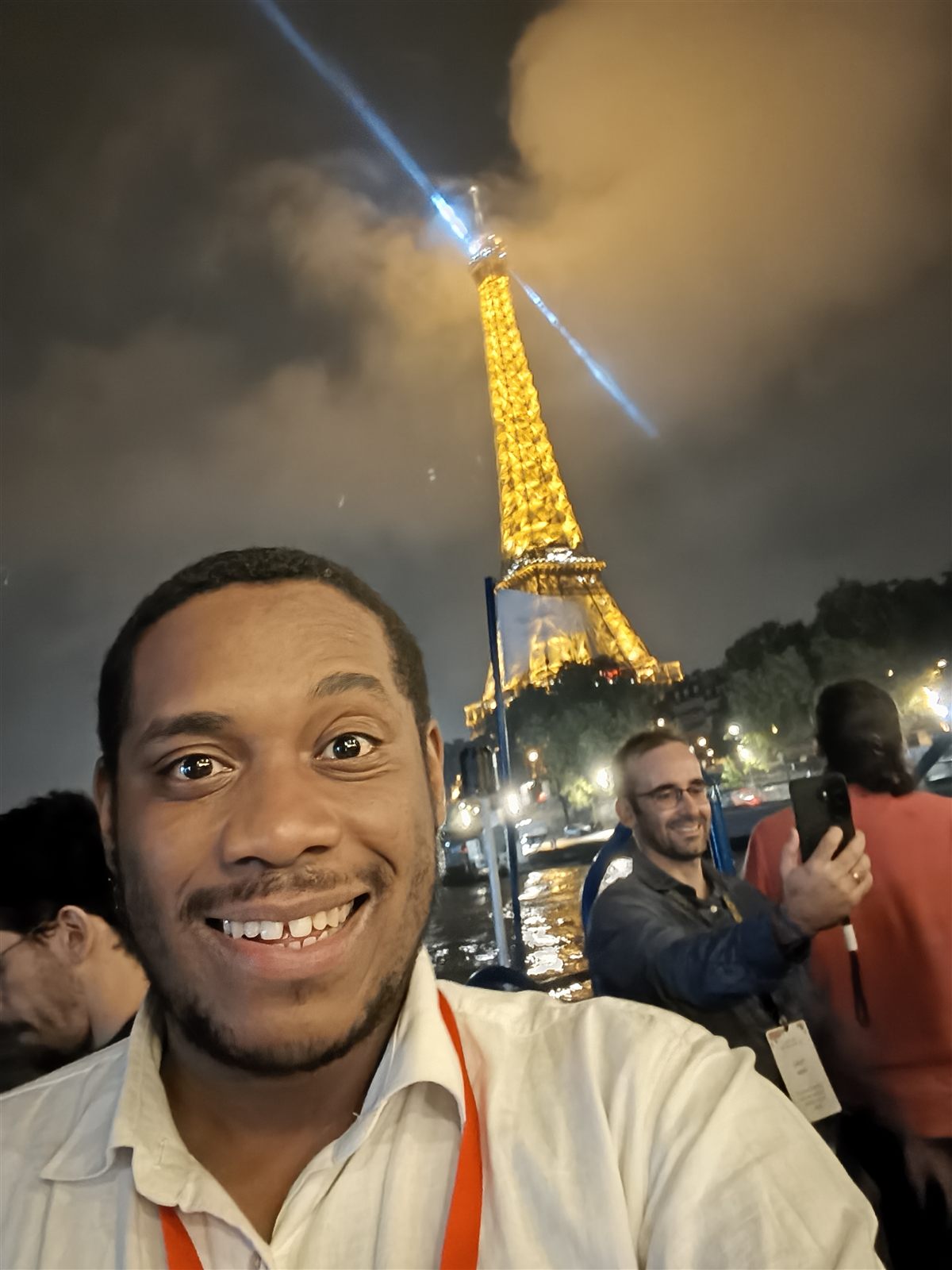 Selfie of Lorenzo on a boat on the Seine at night, with the lit-up Eiffel Tower behind him